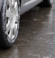 One car tire rests on a patch of dull, black ice.